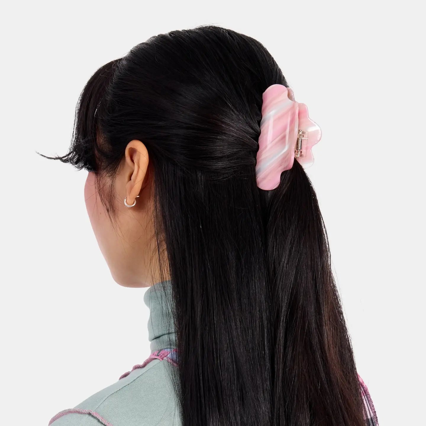 Person with long black hair wearing a pink hair clip on a white background