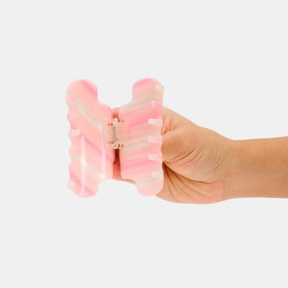 Hand holding a pink and white striped hair clip against a white background