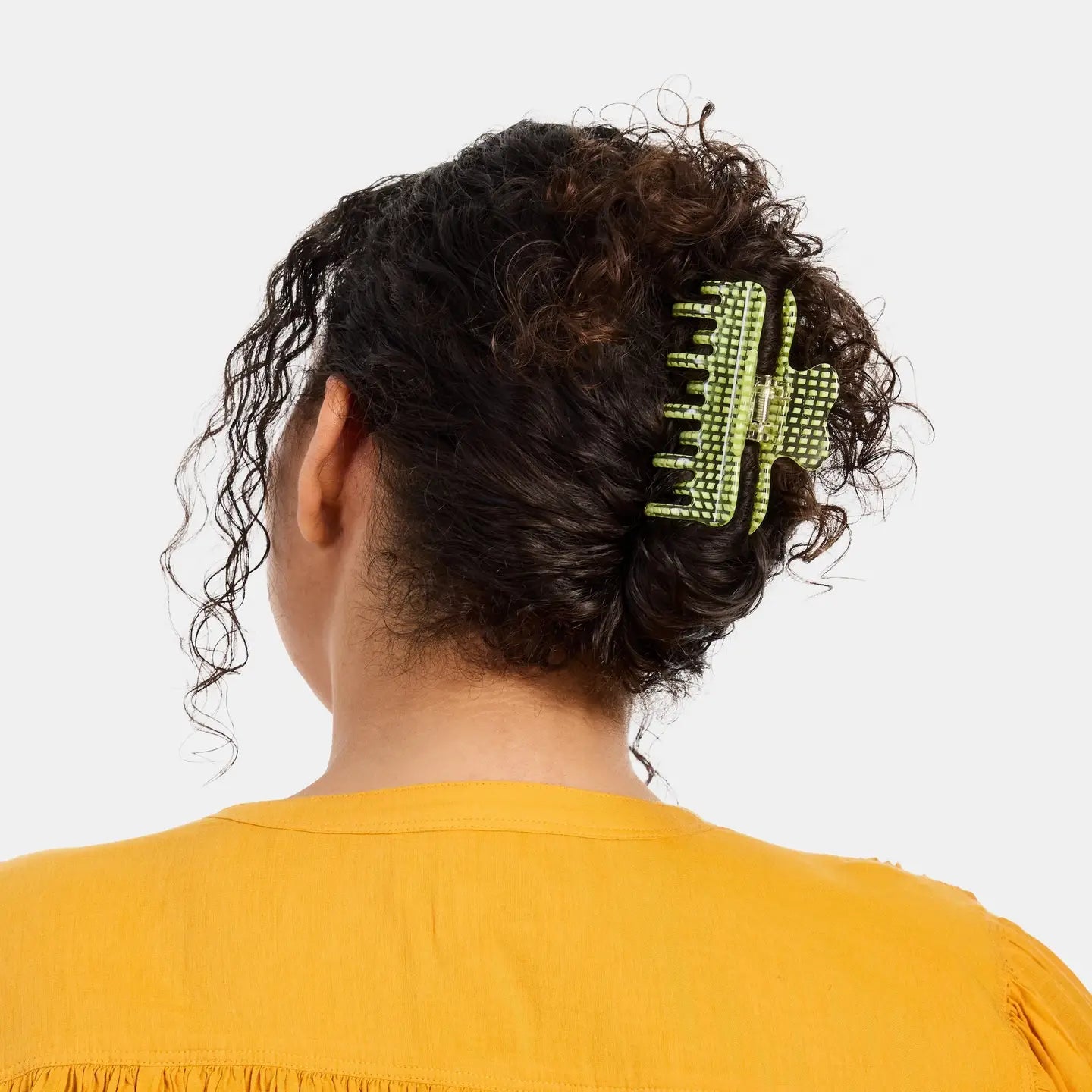 Person with a green hair clip in their curly hair against a white background