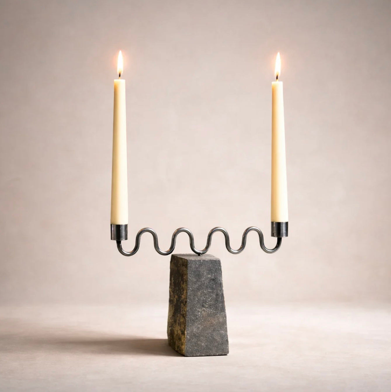 Candle holder with two lit candles on a neutral background