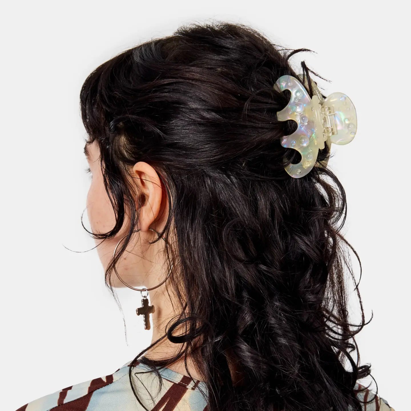 Person with wavy hair wearing a large, iridescent hair clip on a white background