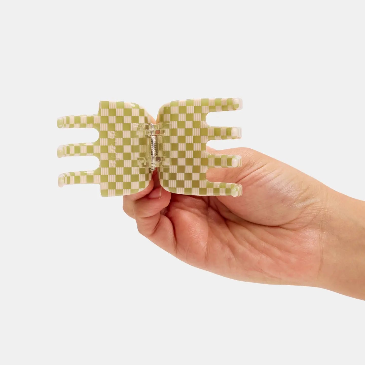Hand holding a green checkered plastic tool against a white background